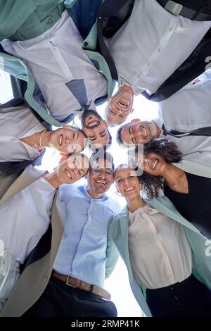 Multiracial diverse group office men women colleagues hugging in circle looking down smiling camera. Stock Photo
