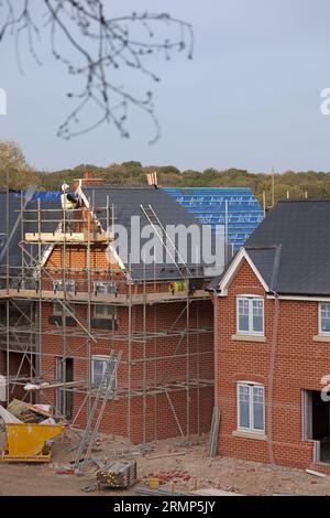 New residential property at various stages of construction: houses with completely finished roofs and part-tiled ones with man working on scaffolding. Stock Photo