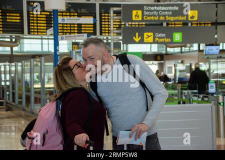 Couple of Caucasian travelers in front of the airport entrance. She gives him a kiss on the cheek Stock Photo