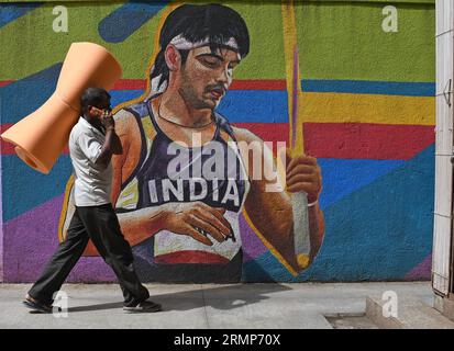 Mumbai, India. 29th Aug, 2023. A man carrying a sponge roll talks on his mobile phone as he walks past a mural painting of Indian track and field athlete Neeraj Chopra in Mumbai. Neeraj Chopra became the first Indian to win gold medal at World Athletics Championship held at Budapest in Hungary. He managed to throw the javelin at a distance of 88.17m which won him the gold medal ahead of Pakistan's Arshad Nadeem who won a silver medal. (Photo by Ashish Vaishnav/SOPA Images/Sipa USA) Credit: Sipa USA/Alamy Live News Stock Photo