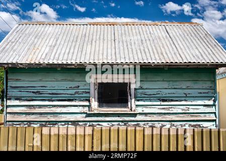 a symmetrical image of a faded, peeling blue painted shed wall with a fence in the foreground Stock Photo