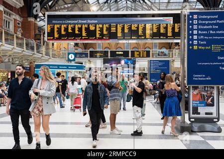 Rail passengers walking through Liverpool Street train station with a welcome sign and train departure times electronic board behind. London, England Stock Photo