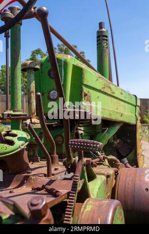 An old, weathered tractor situated in a rural field, with an American flag draped over its back Stock Photo