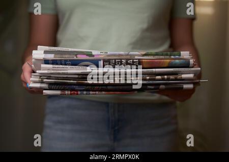 A woman stacks old newspapers in a pile, waste paper collect. Preparing paper waste for recycling. Stock Photo