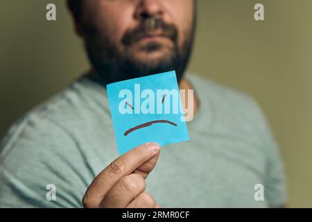 A bearded European man holds a orange sticker in front of him, with a sad smiley Stock Photo