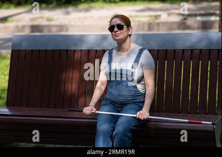 Blind red-haired pregnant woman sitting on a bench outdoors.  Stock Photo