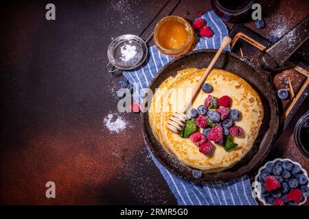 Homemade french tiny pancakes, battercakes with berry. Stack of freshly baked thin crepes on frying pan with fresh blueberry, raspberries and honey. H Stock Photo