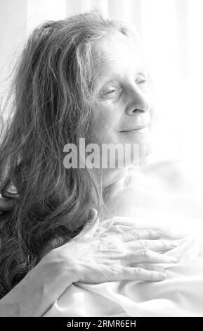 Black and white portrait of a dreamy looking woman of 64 with a light background. Stock Photo
