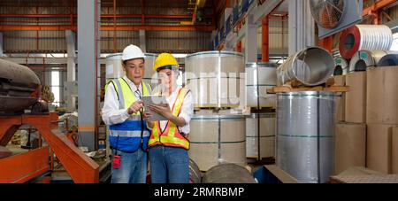 Two diligent workers amidst the dynamic setting of the factory, don the protection of hard hats, indicator of their dedication and the hazards they na Stock Photo