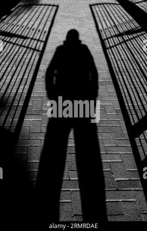 Foreboding shadow of person, legs apart, standing between two semi-open, wrought iron gates Stock Photo