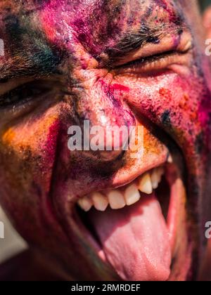 A close up of a painted man with his mouth open, doing silly face with tongue sticking out and one eye winking Stock Photo