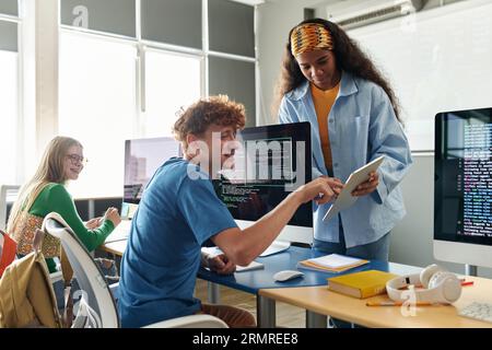 Students using tablet pc and discussing computer program together during IT lesson Stock Photo
