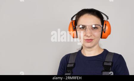 A woman wearing earmuffs and overalls on a white background. Clothing and items for builders, engineer Stock Photo