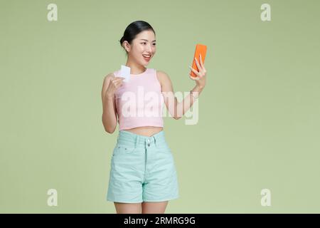 Pleased young woman using mobile phone holding debit card. Stock Photo