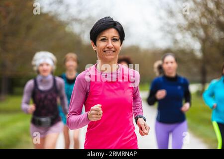 Smiling woman leading a group of female runners training in nature. Concept of physical fitness also in old age. Stock Photo