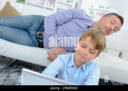 Man looking over shoulder of child using laptop Stock Photo