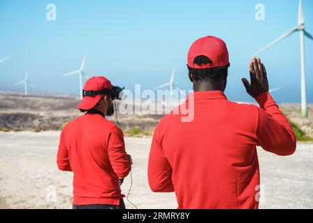 Engineers using virtual reality headset while working at windmill farm with tablet and drone - Focus on african man head Stock Photo