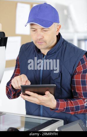 a technician using a tablet to fix a printer Stock Photo