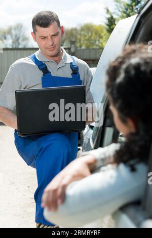 mechanic diagnosing fault in car with laptop Stock Photo