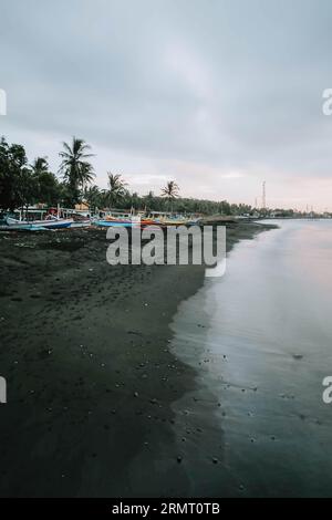 Portrait or vertical of traditional wooden ships or boats are parked on the black sand coastline Stock Photo