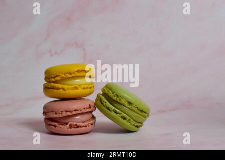 Three yellow, pink and green macarons on pink marble. Stock Photo
