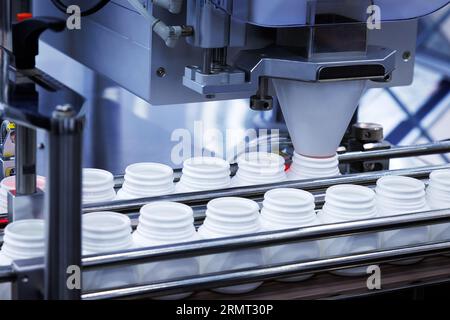 medicine pill capsules are filling in the white plastic bottle on production line machine conveyor at the medical factory. Stock Photo