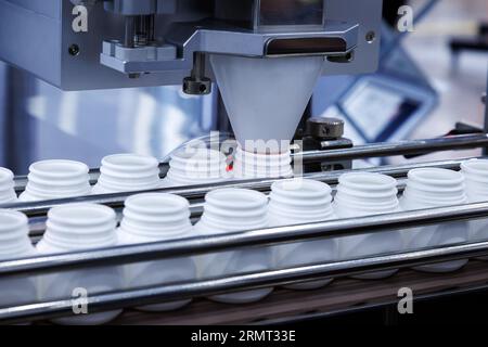 medicine pill capsules are filling in the white plastic bottle on production line machine conveyor at the medical factory. Stock Photo