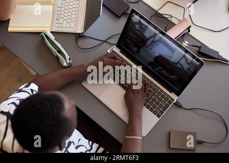 Above view of hands of African American male student typing on laptop keyboard while sitting by desk at informatics lesson and decoding data Stock Photo