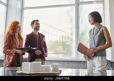 business partners smiling near young architect and building model during presentation in office Stock Photo