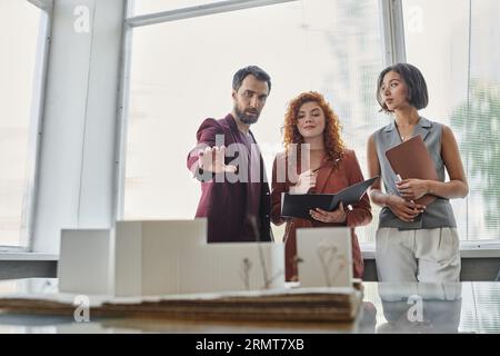 bearded businessman pointing at building model near young female architects, startup presentation Stock Photo