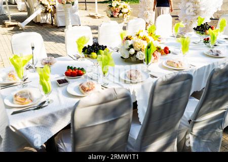 Elegant banquet tables prepared for a conference or a party and covered with a white tablecloth and decorated with flowers for guests Stock Photo