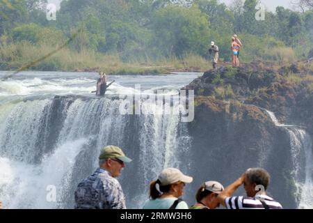 (141002) -- VICTORIA FALLS, -- Foreign tourists pose for photos with local guides at the devil s pool on top of the Victoria Falls, on the borders of Zimbabwe and Zambia, Sept. 30, 2014. The devil s pool is a major site for tourists to the Victoria Falls during the dry season, especially for the months of September and October when the water levels are at the lowest and the current of the Zambezi River is mild. Protected only by the instruction of local guides, swimming in the pool, located on the verge of the 108-meter-high Victoria Falls, has been described as one of the most exciting touris Stock Photo