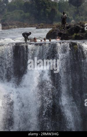 (141002) -- VICTORIA FALLS, -- Foreign tourists pose for photos with local guides at the devil s pool on top of the Victoria Falls, on the borders of Zimbabwe and Zambia, Sept. 30, 2014. The devil s pool is a major site for tourists to the Victoria Falls during the dry season, especially for the months of September and October when the water levels are at the lowest and the current of the Zambezi River is mild. Protected only by the instruction of local guides, swimming in the pool, located on the verge of the 108-meter-high Victoria Falls, has been described as one of the most exciting touris Stock Photo