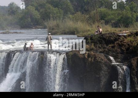 (141002) -- VICTORIA FALLS, -- Foreign tourists pose for photos with local guides at the devil s pool on top of the Victoria Falls, on the borders of Zimbabwe and Zambia, Sept. 30, 2014. The devil s pool is a major site for tourists to the Victoria Falls during the dry season, especially for the months of September and October when the water levels are at the lowest and the current of the Zambezi River is mild. Protected only by the instruction of local guides, swimming in the pool, located on the verge of the 108-meter-high Victoria Falls, has been described as one of the most exciting touris Stock Photo