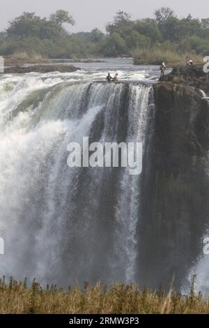 (141002) -- VICTORIA FALLS, -- Foreign tourists pose for photos with local guides at the devil s pool on top of the Victoria Falls, on the borders of Zimbabwe and Zambia, Sept. 30, 2014. The devil s pool is a major site for tourists to the Victoria Falls during the dry season, especially for the months of September and October when the water levels are at the lowest and the current of the Zambezi River is mild. Protected only by the instruction of local guides, swimming in the pool, located on the verge of the 108-meter-high Victoria Falls, has been described as one of the most exciting touris Stock Photo