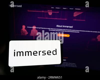 Person holding smartphone with logo of US virtual reality company Immersed Inc. on screen in front of website. Focus on phone display. Stock Photo