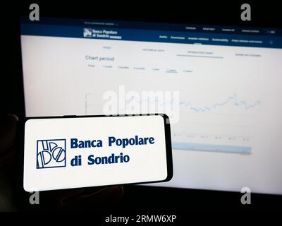 Person holding mobile phone with logo of Banca Popolare di Sondrio SCpA (BPSO) on screen in front of business web page. Focus on phone display. Stock Photo
