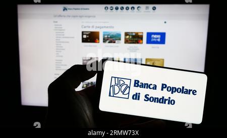 Person holding smartphone with logo of Banca Popolare di Sondrio S.C.p.A. (BPSO) on screen in front of website. Focus on phone display. Stock Photo