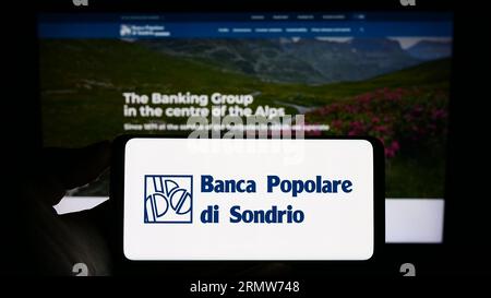 Person holding cellphone with logo of Banca Popolare di Sondrio S.C.p.A. (BPSO) on screen in front of business webpage. Focus on phone display. Stock Photo