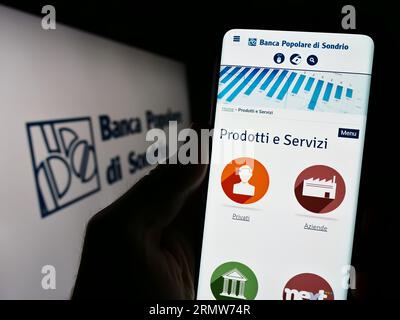 Person holding cellphone with website of Banca Popolare di Sondrio S.C.p.A. (BPSO) on screen in front of logo. Focus on center of phone display. Stock Photo