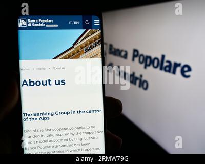 Person holding mobile phone with web page of Banca Popolare di Sondrio SCpA (BPSO) on screen in front of logo. Focus on center of phone display. Stock Photo