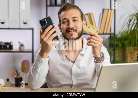 Bearded businessman programmer software developer working making online purchase payment shopping with credit bank card and use laptop at home office desk with laptop. Lebanese freelancer business man Stock Photo