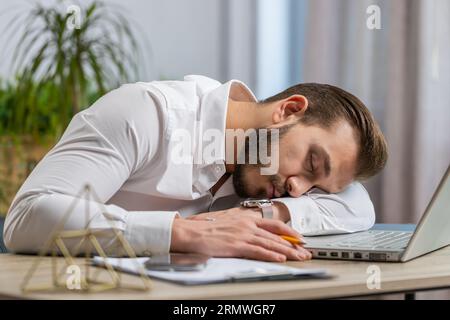 Bored sleepy middle eastern businessman worker working on laptop computer, leaning on hand falling asleep at office. Exhausted tired freelancer workaholic lebanese man. Employment, occupation workless Stock Photo
