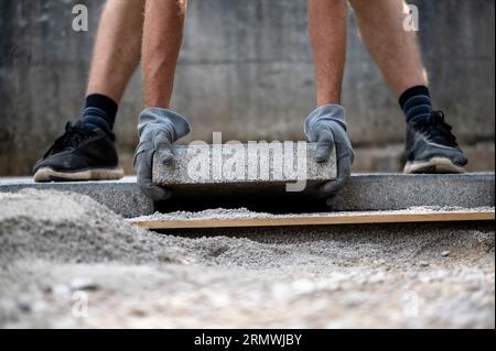 Low angle view of a man a worker wearing protective working gloves placing cement tile on a prepared surface while aving an outdoor patio. DIY project Stock Photo