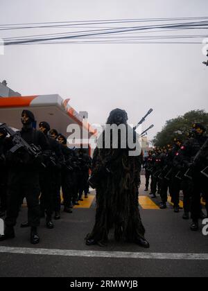 Lima, Peru - July 29 2023: Young Peruvian Man Painting Black Wearing Camouflage Clothing of Bushes and Dirt, Holding a Gun in the Independence Day Mil Stock Photo