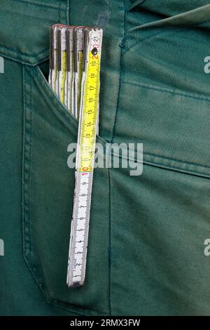 Be moderate. A folding rule made of wood is in the pocket of a pair of green work trousers. Stock Photo