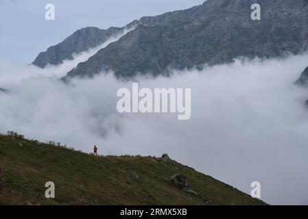 The eastern massif of the Picos de Europa, northern Spain, from the Puertos de Aliva, with cloud hiding the lower slopes. A lone walker provides scale Stock Photo
