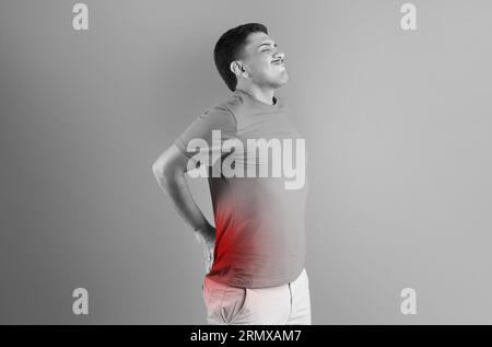 Brazilian man touching aching lower back with red spot on spine, suffering from pain, black and white photo Stock Photo
