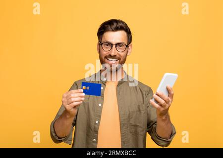 Virtual banking, e-commerce. Happy european middle aged man with smartphone and bank credit card in his hands Stock Photo