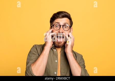 Frightened funny middle aged man touching cheeks, being afraid and screaming, looking at camera on yellow background Stock Photo